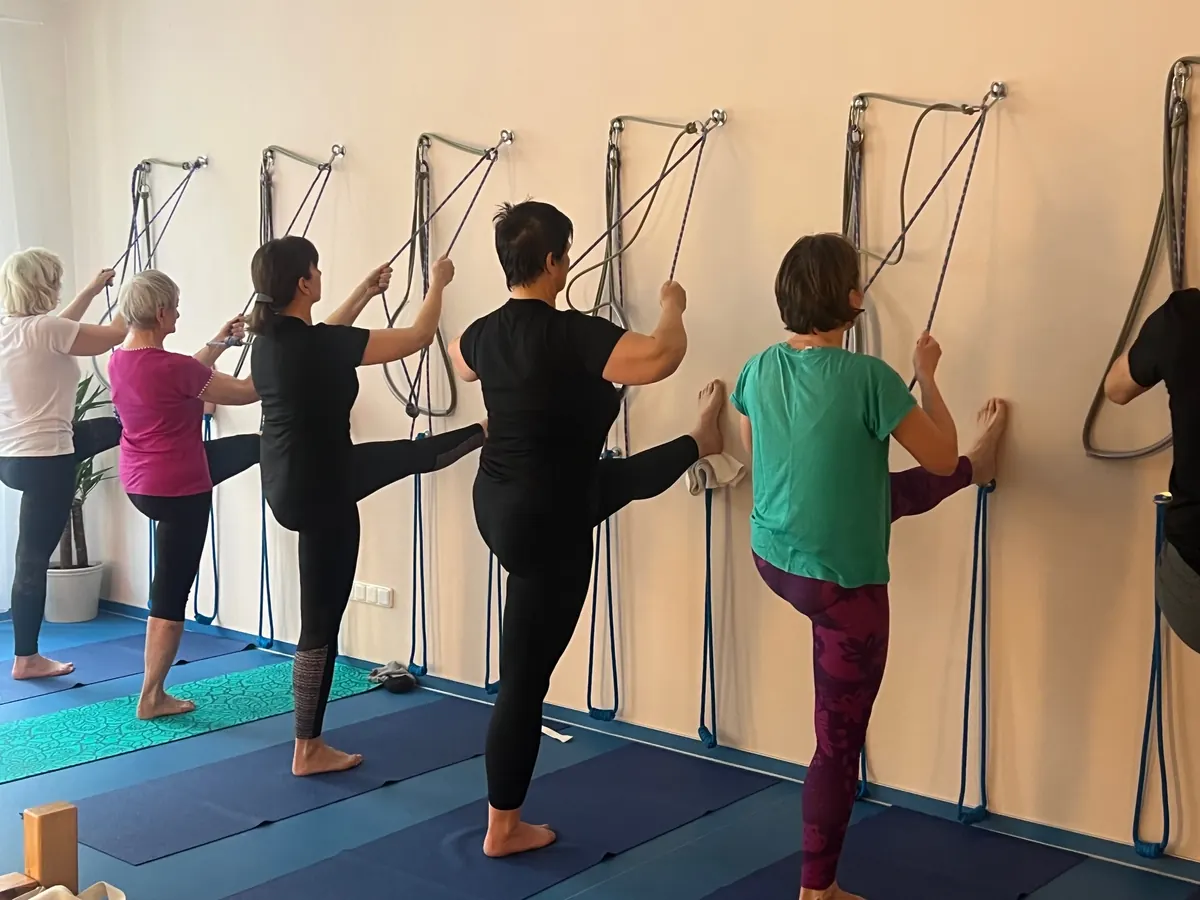 Cvičící ve studiu TaYoga v protažení s nohou opřenou o stěnu, v rukou drží jógová lana